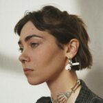 Side profile portrait of a woman with unique ear and neck accessories in soft lighting.